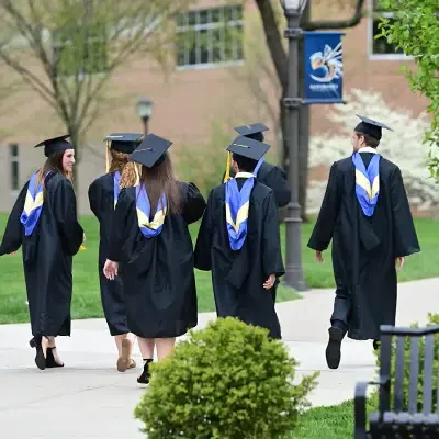 Students in graduation gowns talking 和 walking down the sidewalk